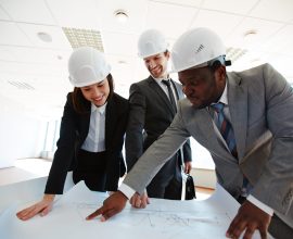 Confident architects in protective helmets looking at blueprint
